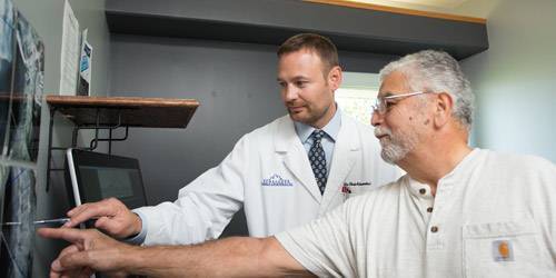 Chiropractor Chris Schroeder Pointing To A Patients X-Ray With The Patient