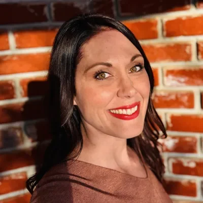 Chiropractic Wichita KS Nicole Schroeder Meet The Team Nicole Schroeder Smiling In Front Of Brick Wall